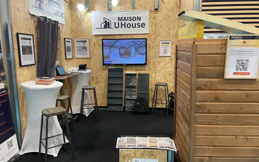 Stand UHouse au salon de l'habitat viving à Reims en 2025. Le stand est composé d'une structure UHouse en panneaux acier / bois osb, et de supports de communication mettant en avant leurs offres du studio de jardin à la maison de plain-pied de 100m²